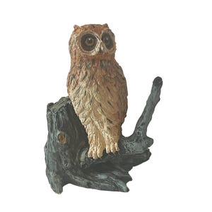 May include: A brown and white owl figurine perched on a grey tree stump. The owl has large, dark eyes and detailed feathers.