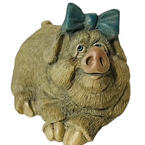May include: A detailed figurine of a pig with a teal bow on its head. The pig has a light brown, textured coat, a pink snout, and blue eyes. The figurine is a decorative item.