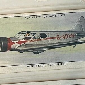 May include: A vintage Player's Cigarettes trading card featuring a white and red airplane with the registration number G-ABXN. The plane is labeled "Airspeed "Courier"".
