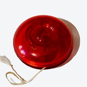 Puede incluir: Un yoyo de plástico rojo con una cuerda blanca.