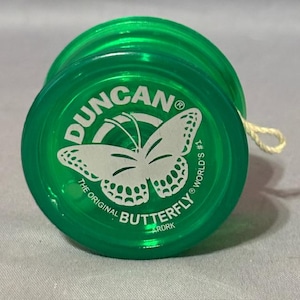 May include: A green Duncan Butterfly yo-yo with a white butterfly graphic and the text "DUNCAN" and "THE ORIGINAL BUTTERFLY". The yo-yo has a string attached and is a classic toy.