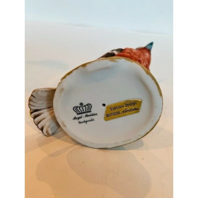 K&ouml;nnte beinhalten: Eine Porzellanfigur eines Rotkehlchens mit wei&szlig;em Schwanz. Die Figur ist mit "Royal Meridion Handgemalt" und "Exklusiv Design DEUTSCHE Noritake" gekennzeichnet.