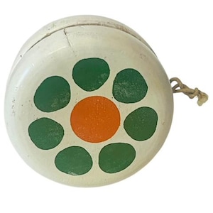 May include: A white wooden yo-yo with a green and orange flower design. The yo-yo has a string attached to it.
