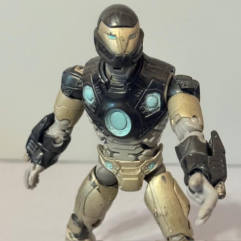 May include: Black and gold action figure of Iron Man in a futuristic suit. The figure has a detailed design with a black helmet and a gold chest plate.