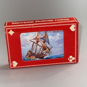 Puede incluir: Una taza de cerámica blanca con asa negra y el texto "But First, Coffee" en negrita negra. La taza se encuentra sobre un fondo borroso, sugiriendo un ambiente acogedor.