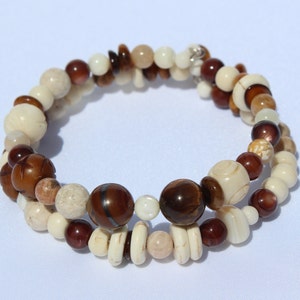 May include: A wrap bracelet featuring a mix of natural beads in shades of brown, cream, and tan. The bracelet includes round, oval, and irregular shaped beads, creating a layered effect. The bracelet is approximately 7 inches in circumference.