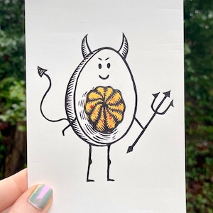 May include: A black and white illustration of a devil egg with a yellow and red yolk. The egg has a devil tail and horns and is holding a pitchfork.