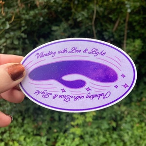 May include: Purple and white sticker with a galaxy-like design and the text "Vibrating with Love & Light" and " Pulsating with Love & Light".