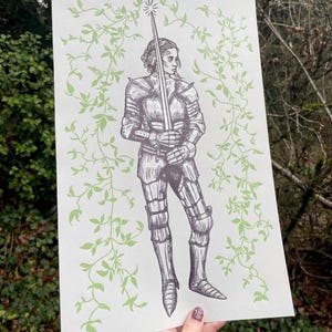 May include: A black and white illustration of a woman in armour holding a sword. The background is a light green with a vine pattern.