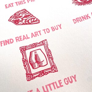 May include: A white paper with red and purple text and illustrations. The text includes phrases like "Eat This Pie" and "Find Real Art to Buy." Illustrations include a pie slice, an eye, and a framed image of a butt.