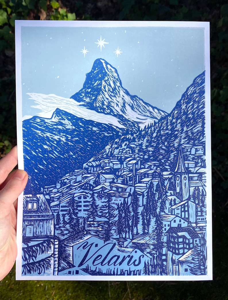 May include: A blue and white linocut print of a mountain village with a church steeple and the text "Velaris" at the bottom. The mountain is snow-capped and there are stars in the sky.