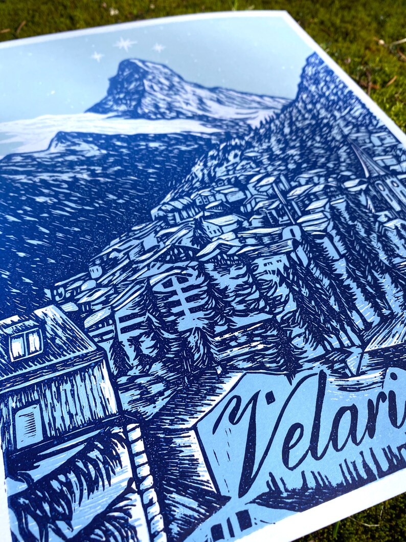 May include: A blue and white linocut print of a mountain village with the word "Velari" in the foreground.