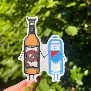 May include: A sticker depicting a cartoon beer bottle and a can, both with smiling faces and holding hands. The bottle is orange with a crest, and the can is blue and white. The sticker is set against a backdrop of green foliage.