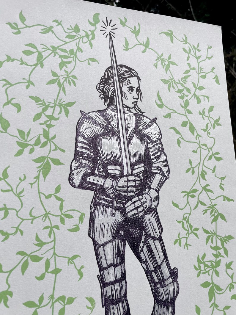 May include: A black and white illustration of a woman in armour holding a sword. The background is a light green with a vine pattern.