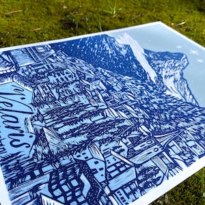 May include: A blue and white linocut print depicting a mountain village with the word "Welcome" in a stylised font.