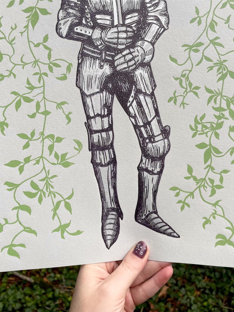 May include: A black and white illustration of a knight in armour standing in front of a green leafy background.