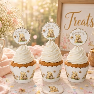 May include: Three cupcakes with white frosting in decorative wrappers featuring a yellow bear and honey pot. Each cupcake has a circular topper with the bear and text reading Mommy To Be or Daddy To Be. The scene includes pink roses and baby's breath.