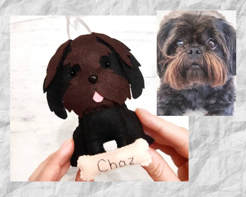 Puede incluir: Un adorno de perro de fieltro marr&oacute;n y negro con la lengua rosa que sobresale. El adorno sostiene un hueso con el nombre "Chaz" escrito en &eacute;l.