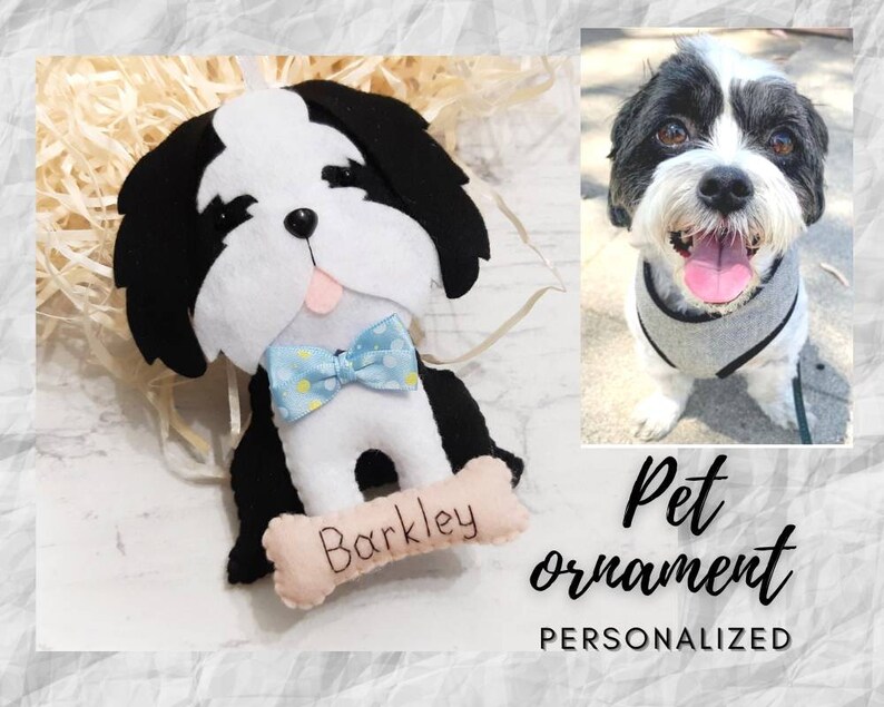 Puede incluir: Adorno de mascota personalizado de fieltro de un perro blanco y negro con una pajarita azul. El adorno tiene una etiqueta en forma de hueso con el nombre "Barkley" escrito en ella.