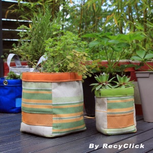 Op de afbeelding: Twee gestreepte stoffen plantenbakken met een oranje rand, een met een groene plant en de andere met een succulent. De plantenbakken staan op een houten dek.