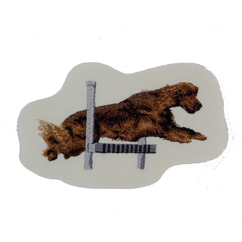 May include: Embroidered patch of a brown dog jumping over a gray hurdle. The dog is in mid-air, with its legs extended and its head tilted forward. The hurdle is a simple, two-bar design.