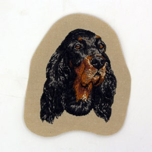 May include: Embroidered patch of a black and brown Gordon Setter dog's head on a beige fabric background.