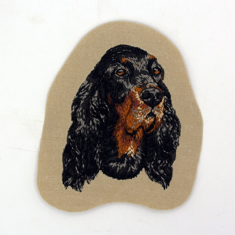 May include: Embroidered patch of a black and brown Gordon Setter dog's head on a beige fabric background.