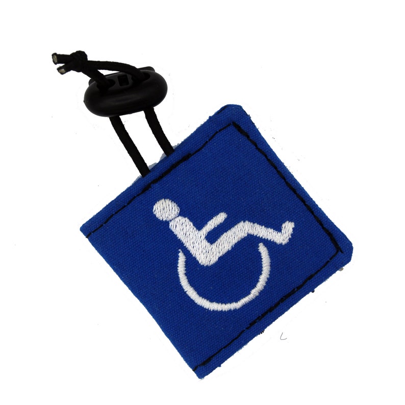 Pu&ograve; includere: Portachiavi in tessuto blu con un simbolo di accessibilit&agrave; in sedia a rotelle ricamato in bianco. Il portachiavi ha un anello elastico nero.
