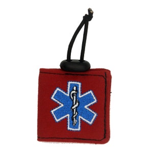 Pu&ograve; includere: Portachiavi in tessuto rosso con un anello elastico nero e un simbolo medico ricamato in blu e bianco.