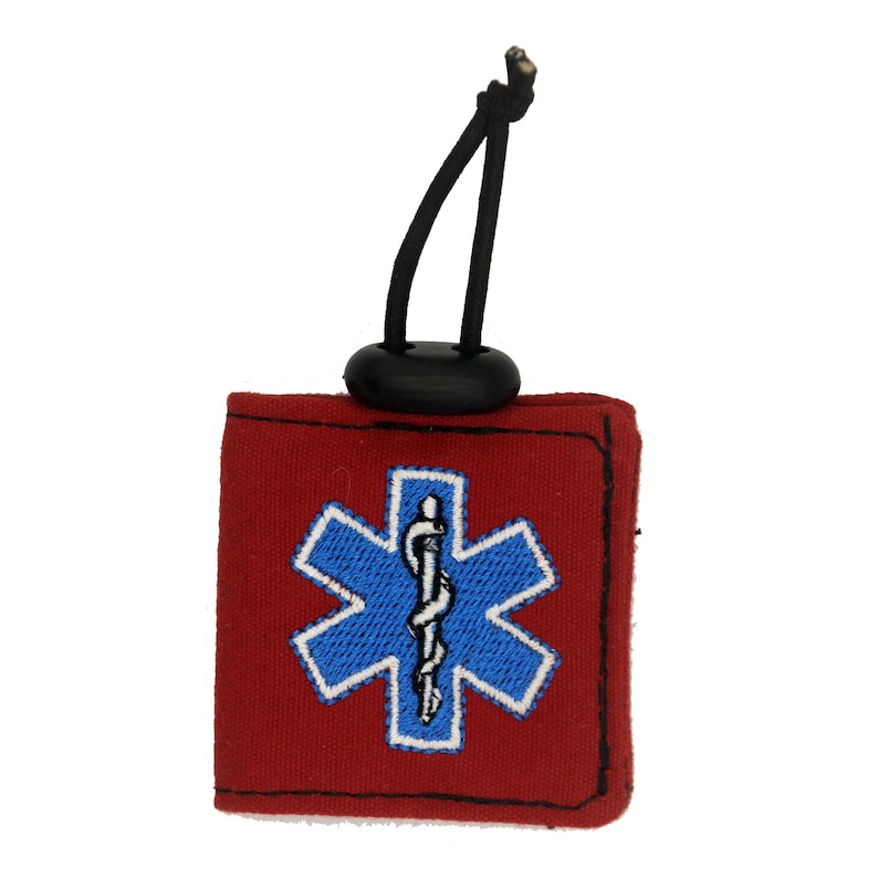 Pu&ograve; includere: Portachiavi in tessuto rosso con un anello elastico nero e un simbolo medico ricamato in blu e bianco.