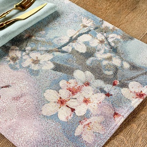 May include: A blue and white placemat with a floral design featuring white flowers with pink centers. The placemat is made of woven fabric and has a textured surface.