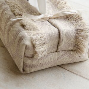 Peut inclure: Un couvre-bo&icirc;te &agrave; mouchoirs beige avec une bordure en franges et un ruban de satin blanc nou&eacute; autour.