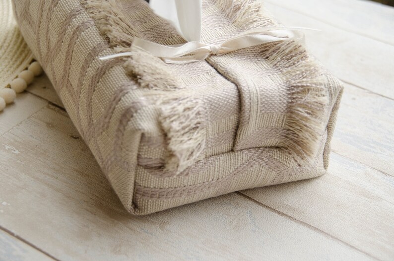 Peut inclure: Un couvre-bo&icirc;te &agrave; mouchoirs beige avec une bordure en franges et un ruban de satin blanc nou&eacute; autour.