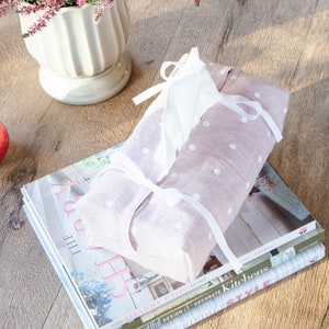 May include: A pink and white polka dot tissue box cover with white ribbon ties. The cover is sitting on top of a stack of home decor magazines.