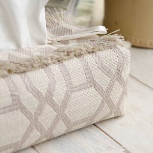 Peut inclure: Un couvre-bo&icirc;te &agrave; mouchoirs beige avec un motif g&eacute;om&eacute;trique et une bordure en franges. Le couvre-bo&icirc;te est orn&eacute; d'un ruban blanc.
