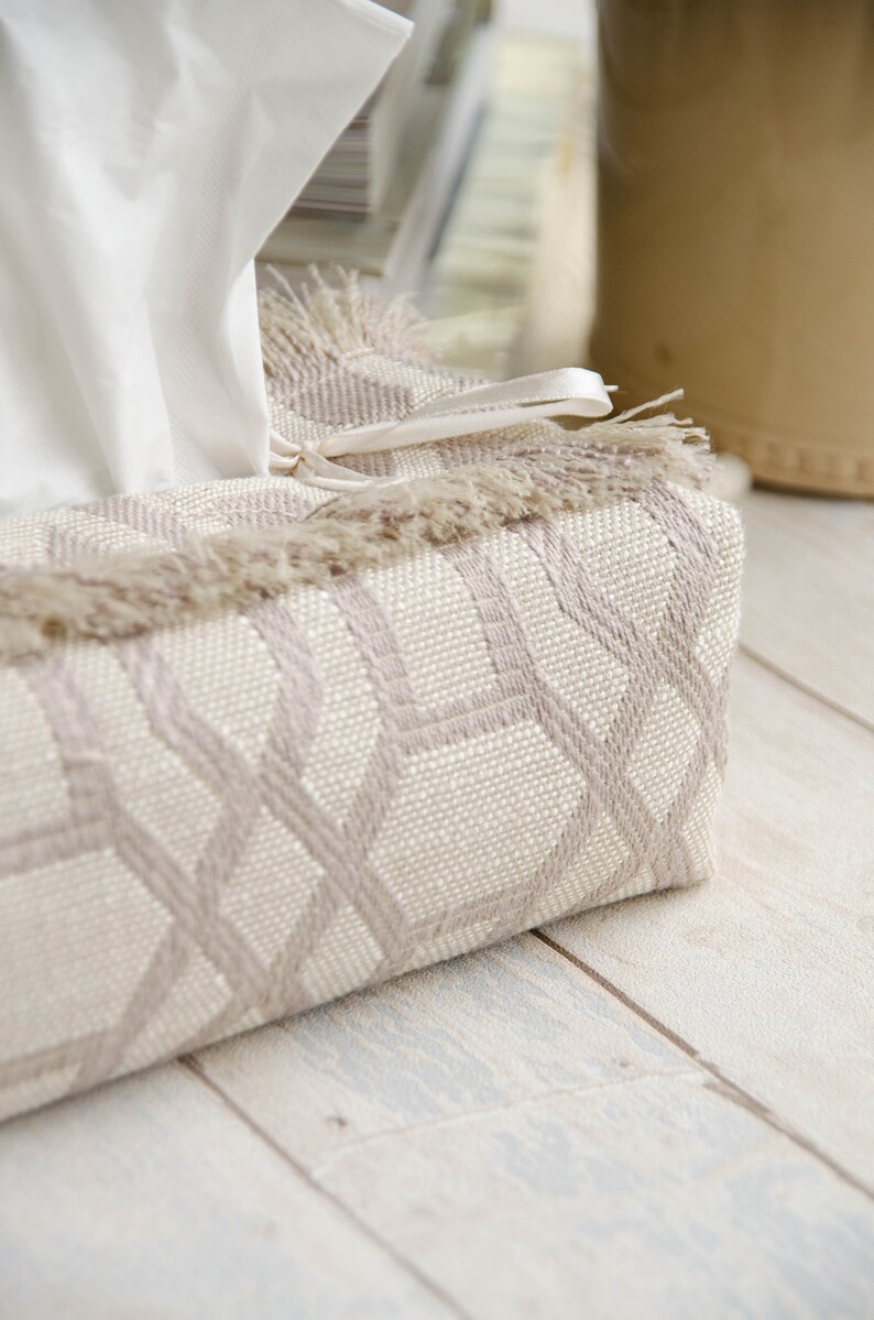 Peut inclure: Un couvre-bo&icirc;te &agrave; mouchoirs beige avec un motif g&eacute;om&eacute;trique et une bordure en franges. Le couvre-bo&icirc;te est orn&eacute; d'un ruban blanc.