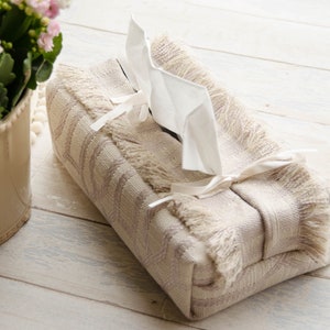 Peut inclure: Un couvre-bo&icirc;te &agrave; mouchoirs beige avec une bordure en franges et un ruban blanc. Le couvre-bo&icirc;te pr&eacute;sente un motif g&eacute;om&eacute;trique subtil et est fait d'un tissu tiss&eacute;.