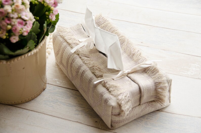 Peut inclure: Un couvre-bo&icirc;te &agrave; mouchoirs beige avec une bordure en franges et un ruban blanc. Le couvre-bo&icirc;te pr&eacute;sente un motif g&eacute;om&eacute;trique subtil et est fait d'un tissu tiss&eacute;.
