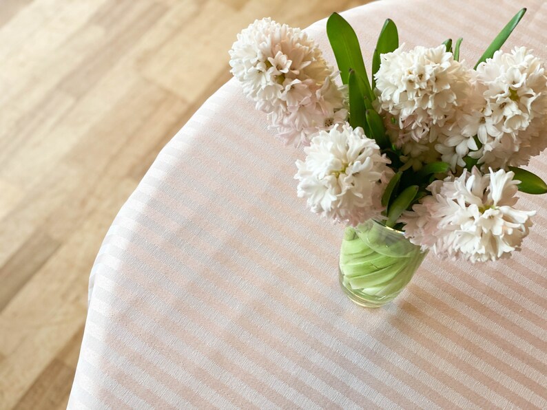 Puede incluir: Un ramo de jacintos rosa p&aacute;lido en un jarr&oacute;n de vidrio transparente sobre un mantel a rayas.