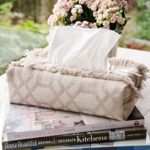 Peut inclure: Un couvre-bo&icirc;te &agrave; mouchoirs beige avec un motif tiss&eacute; et une bordure en franges pos&eacute; sur une pile de livres de d&eacute;coration int&eacute;rieure. Les livres sont intitul&eacute;s "The Shabby Chic Home", "House Beautiful Design & Decorate Kitchens" et "House Beautiful The Home Book".