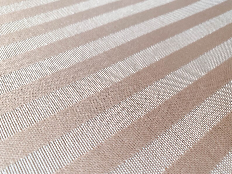 Puede incluir: Primer plano de una tela beige con rayas blancas. La tela tiene una textura sutil y un acabado ligeramente brillante.
