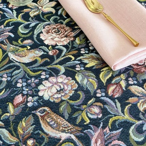 Może przedstawiać: Czarny obrus z kwiatowym i ptasim wzorem tapiserii. Obrus zdobią różowe, żółte i zielone kwiaty oraz brązowe ptaki. Na obrusie leży różowa serwetka lniana i złota łyżka.