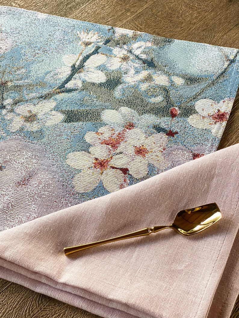 May include: A pink linen napkin with a gold spoon on top. The napkin is folded in half and the spoon is lying on top of the napkin. The spoon is a traditional style with a rounded bowl and a long handle. The napkin is a light pink color and has a soft, textured surface. The spoon is a shiny gold color and has a smooth surface.