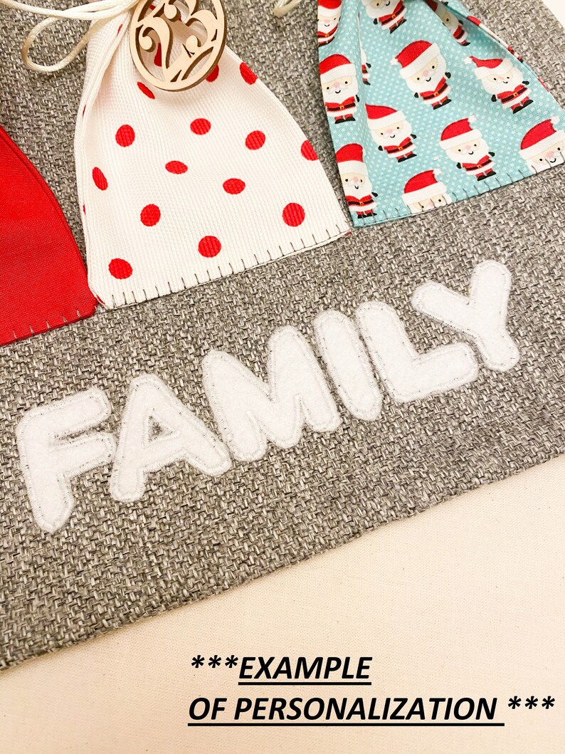 Puede incluir: Un calendario de adviento de arpillera gris con bolsillos de fieltro blanco y la palabra "FAMILY" en letras de fieltro blanco. Los bolsillos est&aacute;n decorados con lunares rojos y blancos, patrones de Pap&aacute; Noel y un adorno de &aacute;rbol de Navidad de madera.