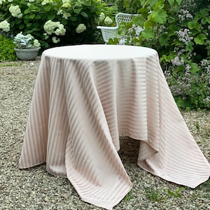 Puede incluir: Un mantel de mesa a rayas rosa y blanco drapeado sobre una mesa redonda en un jard&iacute;n.