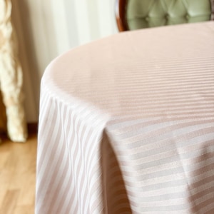 Puede incluir: Primer plano de un mantel de color rosa claro con rayas blancas. El mantel est&aacute; drapeado sobre una mesa redonda.
