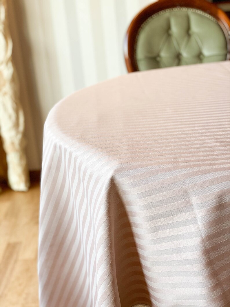 Puede incluir: Primer plano de un mantel de color rosa claro con rayas blancas. El mantel est&aacute; drapeado sobre una mesa redonda.