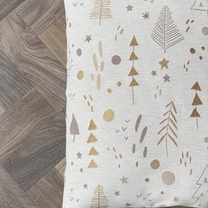 May include: A white throw pillow with a gold and brown pattern of trees, stars, and other abstract shapes.
