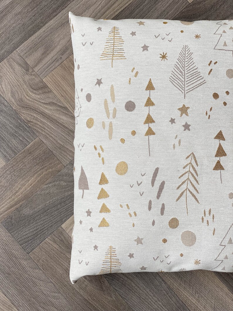 May include: A white throw pillow with a gold and brown pattern of trees, stars, and other abstract shapes.