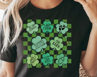 Puede incluir: Camiseta negra con un patrón de trébol verde y texto que dice "At Ur Cervix", "L&D Crew", "Delivering Cute Little Lucky Charms", "Oh Baby", "Lucky L&D Nurse".